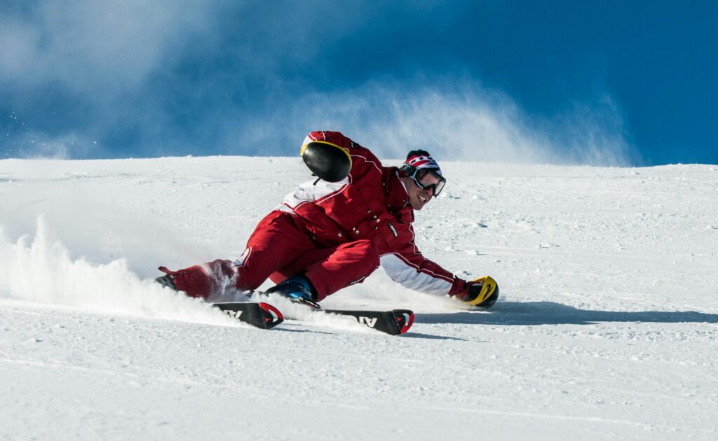 A skier in vibrant red gear skillfully navigates a snowy slope on a sunny day.